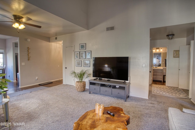 living room featuring ceiling fan, a towering ceiling, visible vents, and light colored carpet