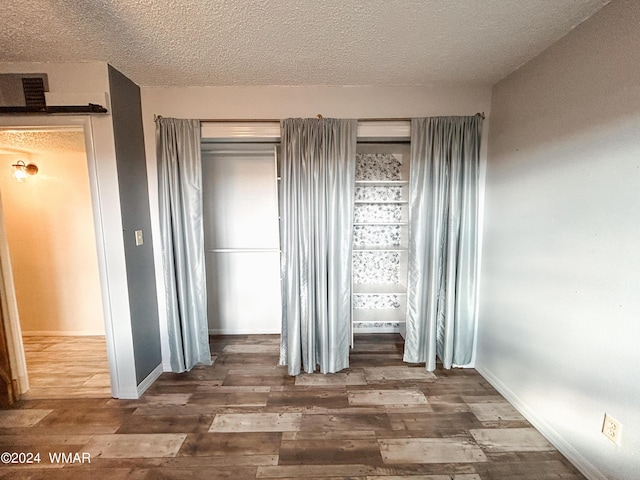 unfurnished bedroom with dark wood-type flooring, a textured ceiling, and baseboards