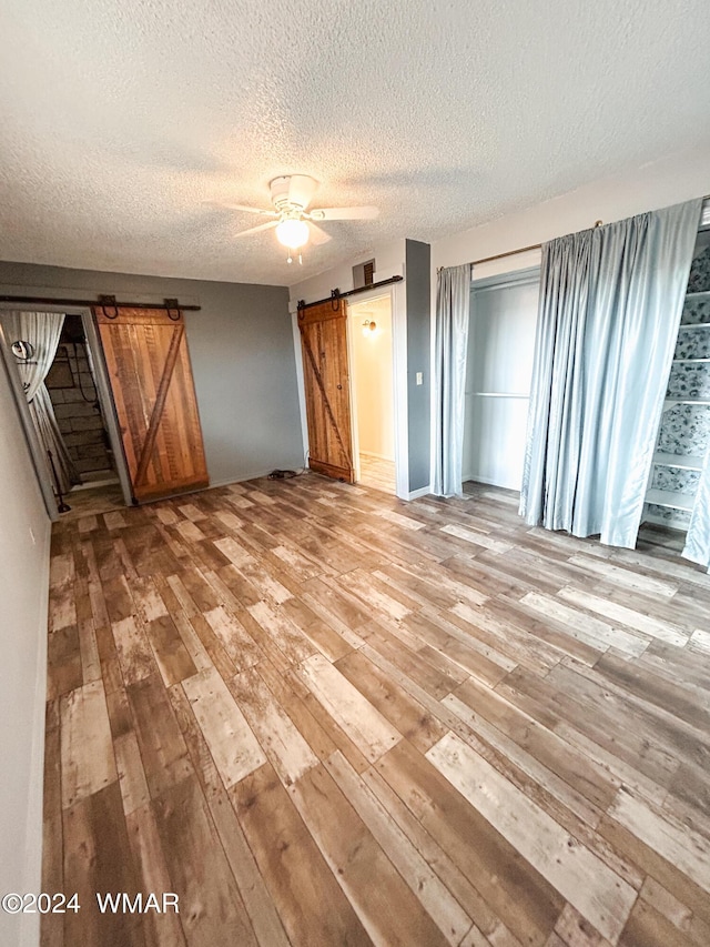 unfurnished bedroom with a textured ceiling, a barn door, a ceiling fan, visible vents, and light wood-style floors