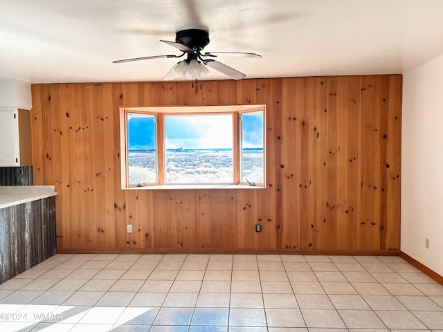 empty room with light tile patterned floors, wooden walls, a ceiling fan, and baseboards