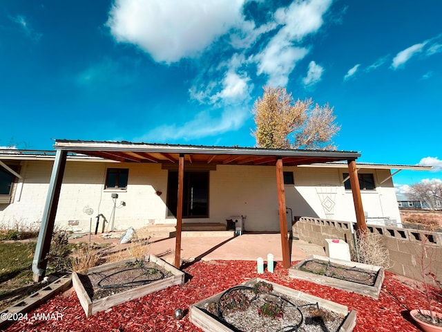 back of house featuring a vegetable garden, concrete block siding, metal roof, fence, and a patio area