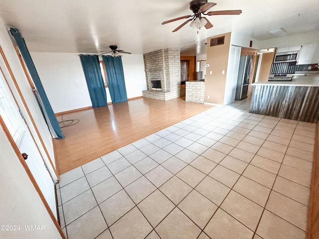 unfurnished living room featuring a fireplace, visible vents, baseboards, light wood-style floors, and a ceiling fan