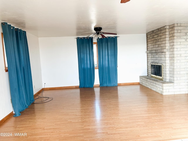 unfurnished living room with baseboards, light wood-type flooring, a ceiling fan, and a brick fireplace