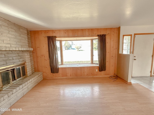 unfurnished living room with baseboards, wood walls, a brick fireplace, and light wood-style floors