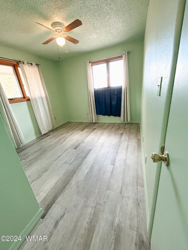 unfurnished room with a textured ceiling, light wood finished floors, and a ceiling fan