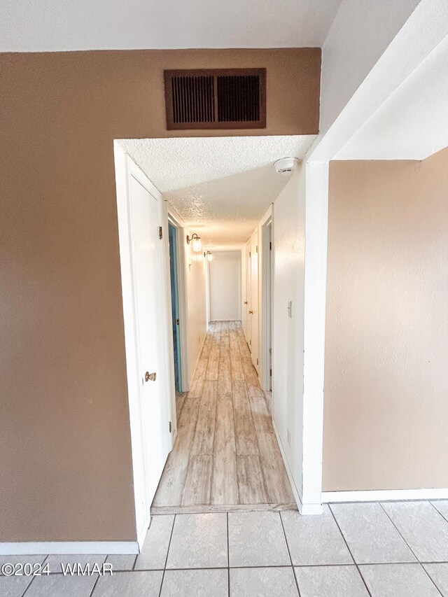 hall with light tile patterned floors, baseboards, visible vents, and a textured ceiling