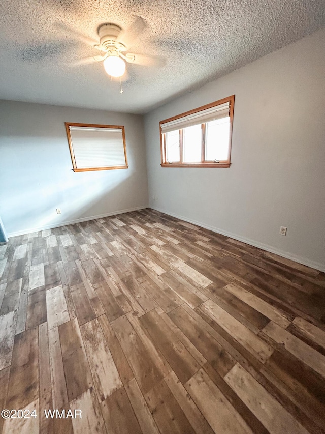 empty room with ceiling fan, a textured ceiling, wood finished floors, and baseboards