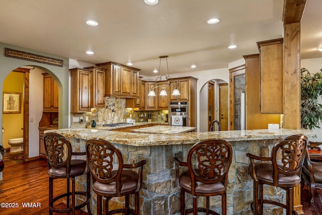 4040 W Ninebark Ln, Show Low, AZ 85901 - kitchen with brown cabinetry, arched walkways, a peninsula, backsplash, and light stone countertops
