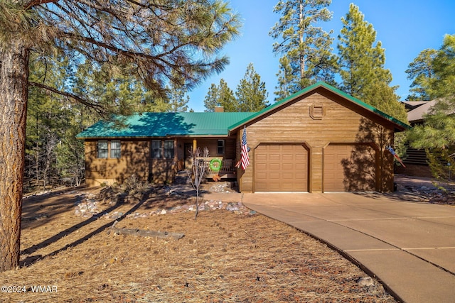 view of front of house with a garage, a chimney, metal roof, and driveway