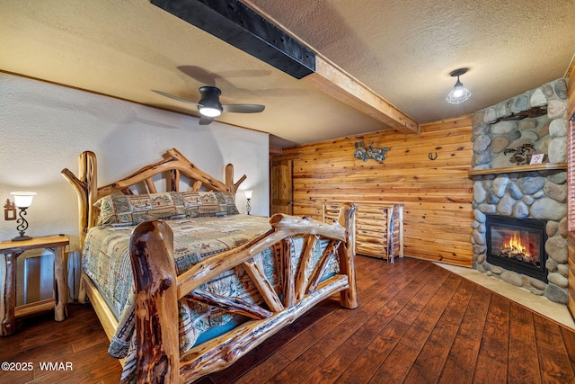 2444 S Jan Ln, Pinetop, AZ 85935 - bedroom with a textured ceiling, hardwood / wood-style floors, beam ceiling, a stone fireplace, and wooden walls
