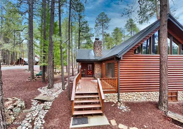 exterior space featuring roof with shingles, a chimney, stone siding, log veneer siding, and a deck