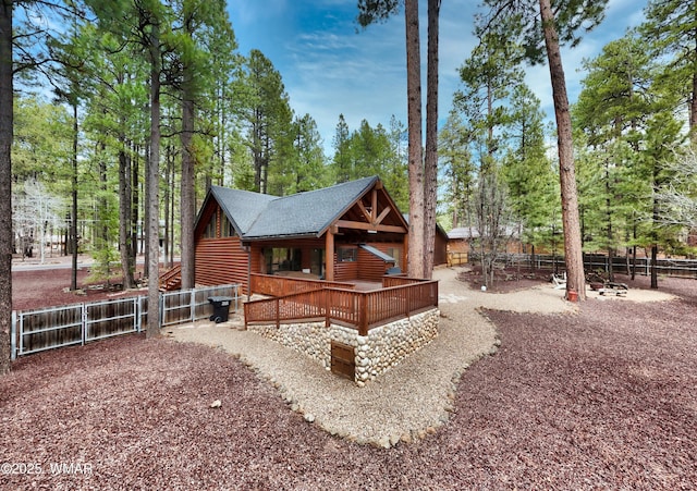 rear view of property featuring a shingled roof, fence, faux log siding, and a gate