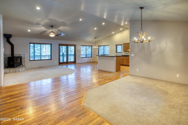 unfurnished living room with light wood-style floors, recessed lighting, a wood stove, and ceiling fan with notable chandelier