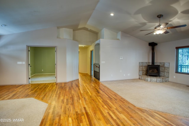 unfurnished living room featuring carpet, a ceiling fan, a wood stove, vaulted ceiling, and wood finished floors