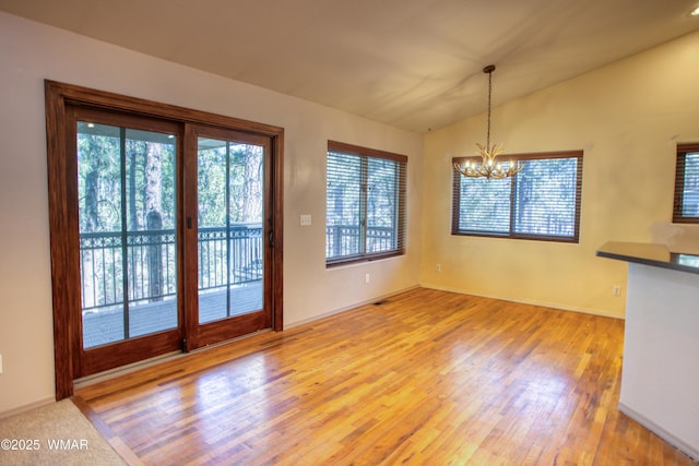 unfurnished dining area with lofted ceiling, light wood finished floors, and an inviting chandelier