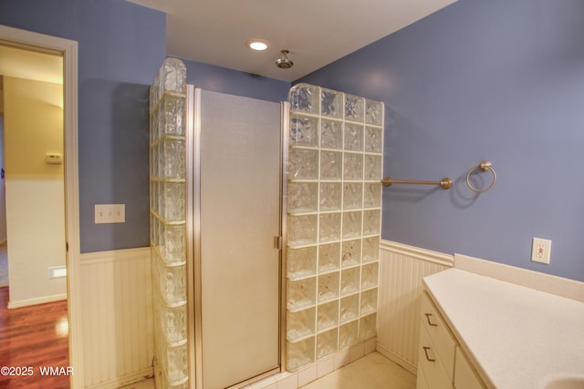 full bathroom featuring vanity, walk in shower, wood finished floors, and wainscoting