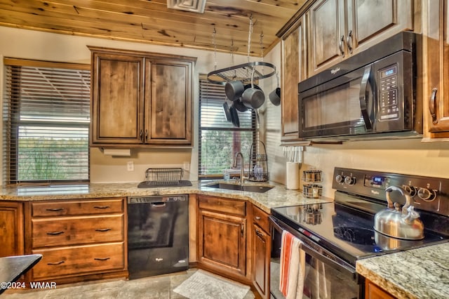 kitchen with brown cabinetry, wooden ceiling, light stone counters, black appliances, and a sink