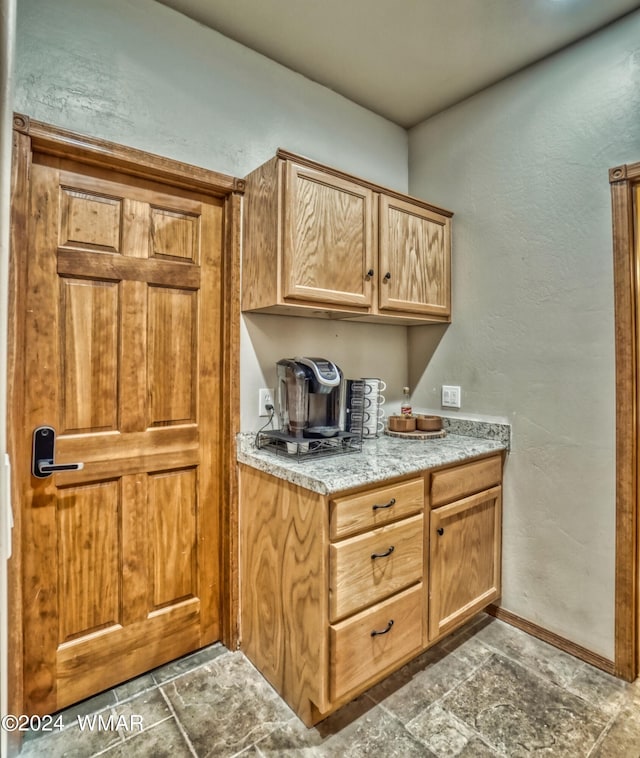 kitchen with baseboards, light countertops, a textured wall, and stone tile floors