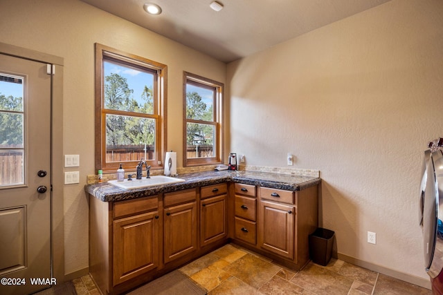 kitchen with dark countertops, brown cabinetry, stone finish floor, a sink, and baseboards