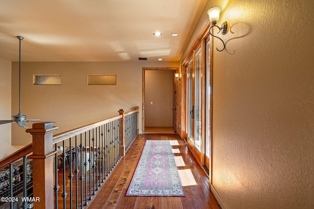 corridor with a textured wall, wood finished floors, and visible vents