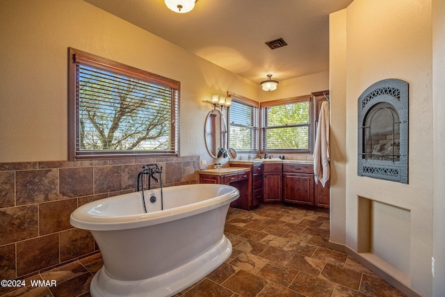 full bath with tile walls, a soaking tub, visible vents, stone finish flooring, and vanity