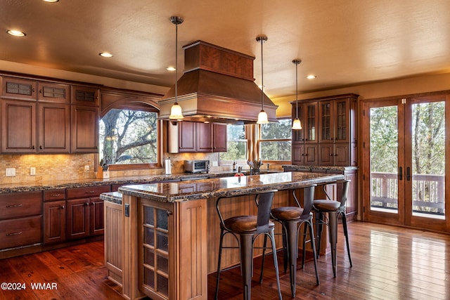 kitchen with decorative light fixtures, a kitchen island, dark wood-style floors, dark stone countertops, and glass insert cabinets