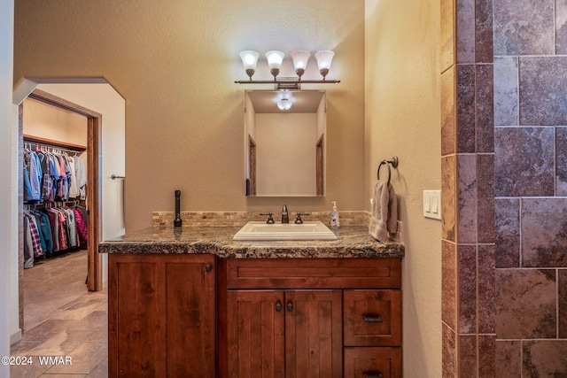 full bath featuring a textured wall, a spacious closet, and vanity
