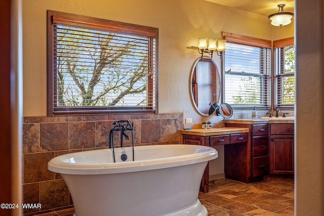 bathroom featuring a textured wall, vanity, tile walls, a freestanding bath, and stone finish flooring