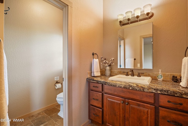 half bathroom featuring toilet, stone finish flooring, baseboards, and vanity