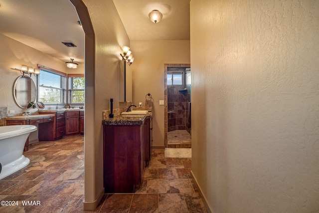 full bathroom featuring two vanities, a textured wall, a stall shower, stone finish floor, and baseboards