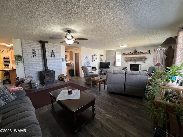 living area with a ceiling fan, dark wood-style floors, brick wall, a wood stove, and a fireplace