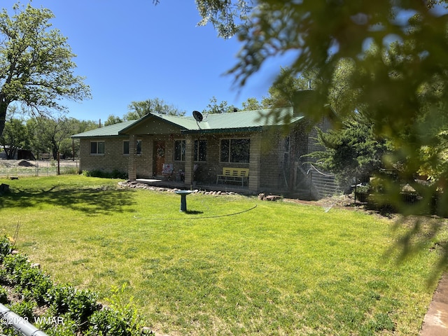 single story home featuring metal roof, brick siding, a front yard, and fence