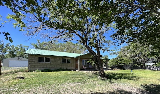 exterior space with metal roof, brick siding, a detached garage, fence, and a lawn