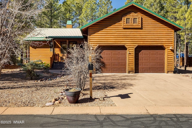 cabin featuring metal roof, a garage, driveway, faux log siding, and a chimney