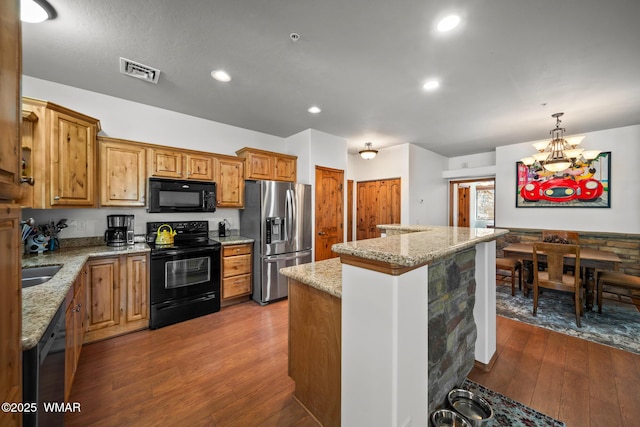 kitchen with visible vents, a center island, light stone counters, hardwood / wood-style flooring, and black appliances