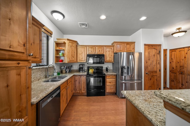 kitchen featuring light wood finished floors, visible vents, light stone countertops, black appliances, and a sink