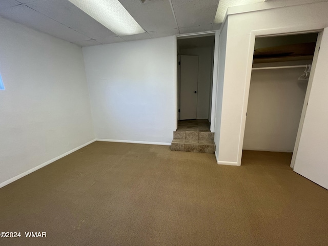 unfurnished bedroom with a paneled ceiling, carpet, baseboards, and a closet