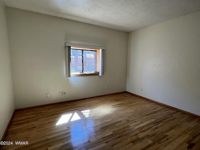 unfurnished room featuring a textured ceiling, wood finished floors, and baseboards