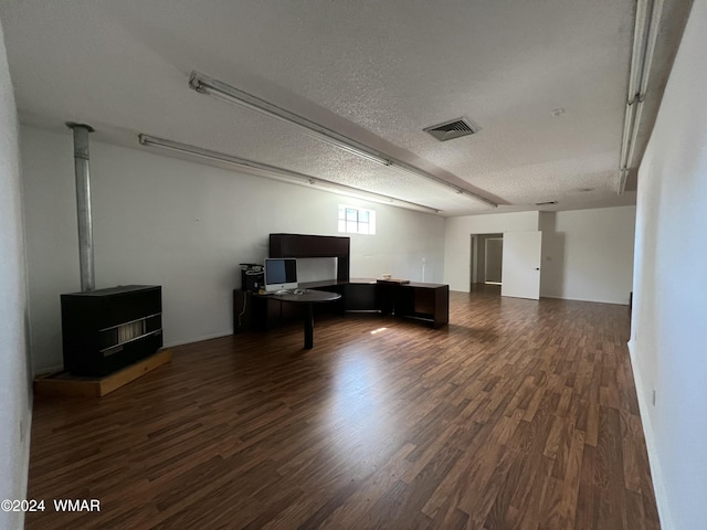 living area with dark wood-style floors, a wood stove, visible vents, and a textured ceiling