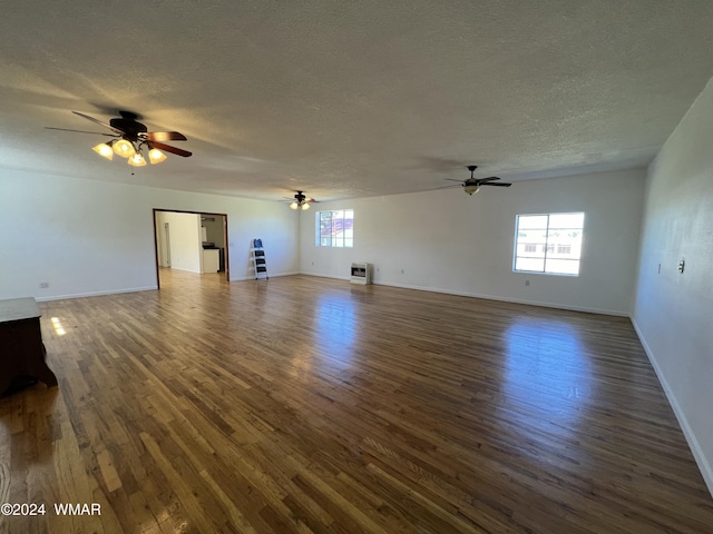 unfurnished living room featuring a textured ceiling, ceiling fan, baseboards, heating unit, and dark wood finished floors