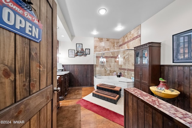 bathroom featuring a bath, a wainscoted wall, wood walls, and a tile shower