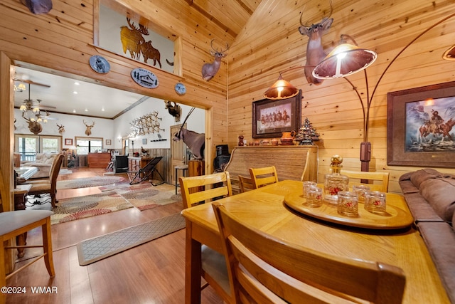 dining area with wood finished floors, high vaulted ceiling, ceiling fan, wood walls, and crown molding