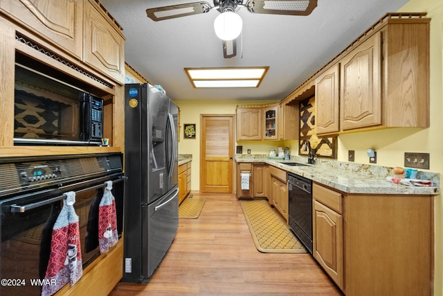 kitchen featuring a sink, black appliances, light countertops, glass insert cabinets, and light wood-style floors