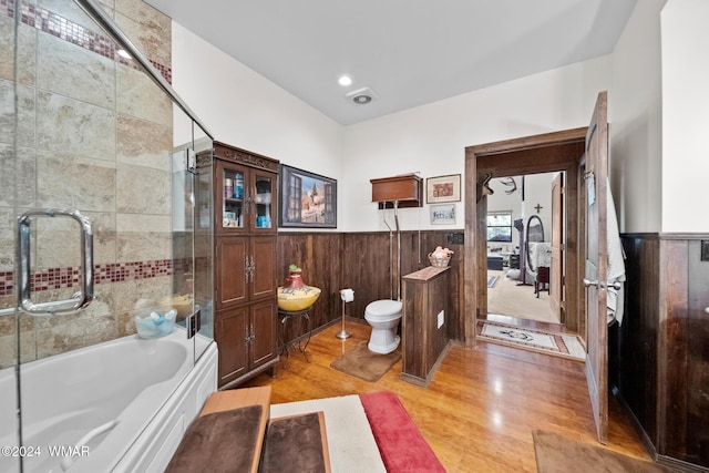 bathroom with toilet, ensuite bath, wood finished floors, wooden walls, and wainscoting