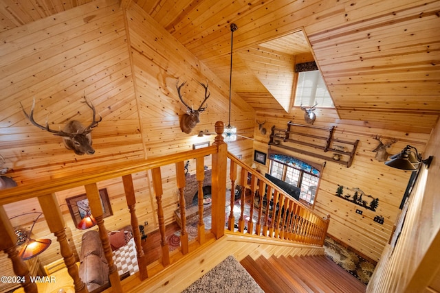 stairway with wood finished floors, high vaulted ceiling, wooden ceiling, and wooden walls