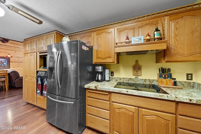 kitchen with wooden walls, black electric stovetop, light stone counters, light wood-style flooring, and stainless steel fridge