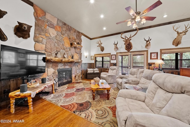 living area with a wainscoted wall, ornamental molding, a stone fireplace, wood finished floors, and a ceiling fan