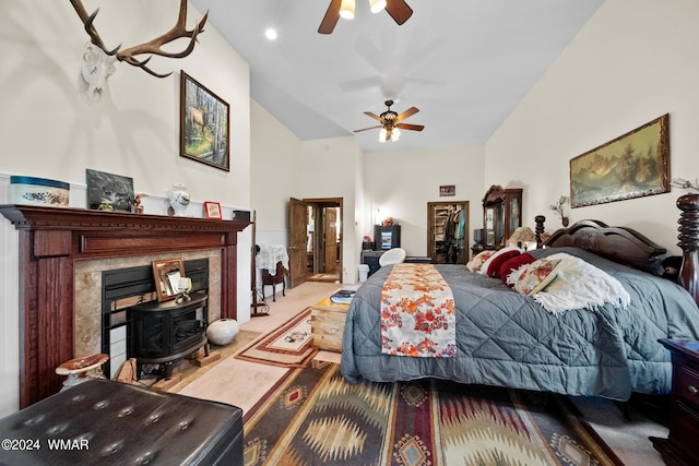 carpeted bedroom featuring ensuite bath, high vaulted ceiling, a wood stove, and a ceiling fan