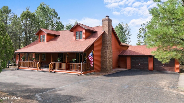 view of front of property with a chimney, roof with shingles, covered porch, and driveway