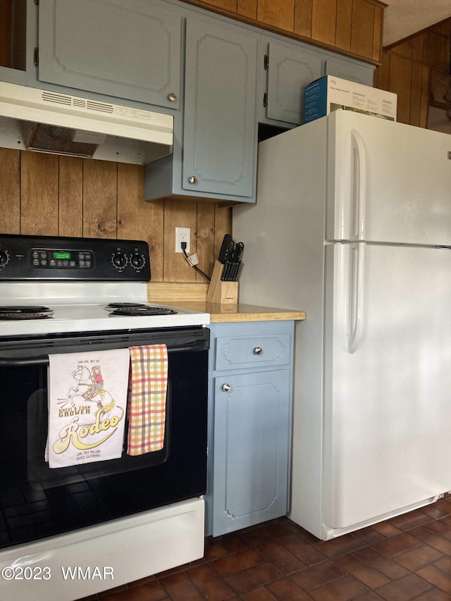 kitchen with brick floor, under cabinet range hood, electric range, light countertops, and freestanding refrigerator